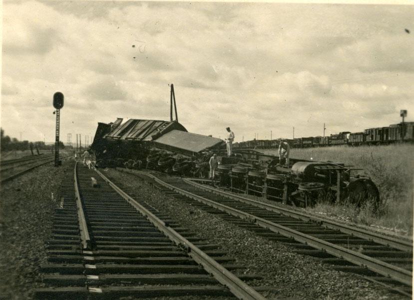 Sur une voie ferrée, ouvriers autour d'un train de munitions déraillé